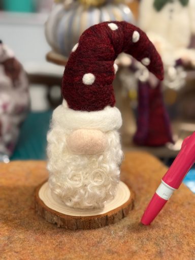 A felted Santa figure with a red polka-dotted hat, sitting on a wooden base.