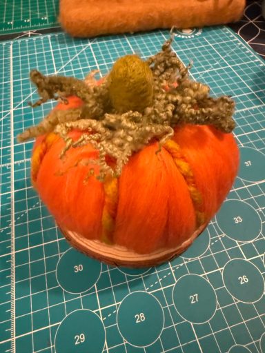 A decorative pumpkin with green foliage on a round wooden base.