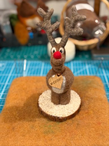 Brown felt reindeer figurine with a red nose, standing on a wooden base.