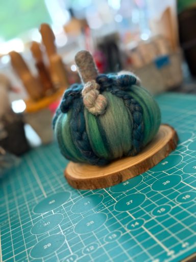 A teal and blue decorative pumpkin on a wooden base, set on a crafting mat.