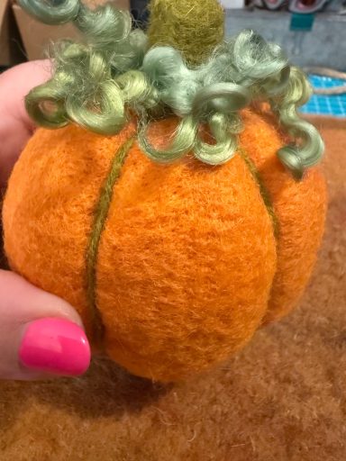 A small, orange felt pumpkin with green curly decoration on top.