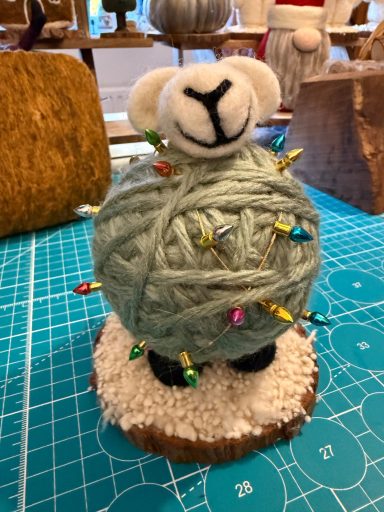 A decorative sheep atop a yarn ball with colourful pins on a wooden base.