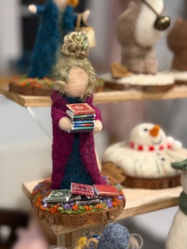 A crafted figure holding books, adorned in vibrant clothing, surrounded by decorative details.