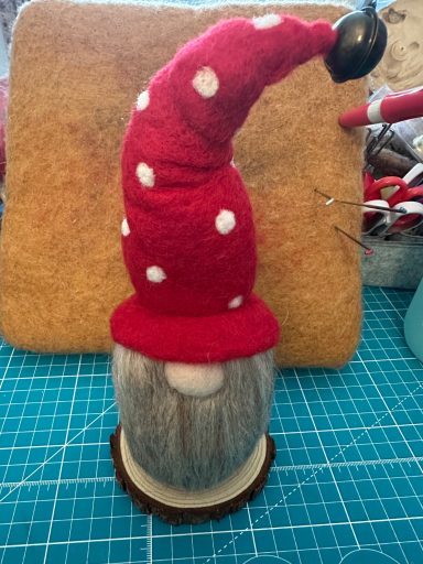 A gnome with a grey beard and a red, polka-dotted hat, perched on a wooden base.