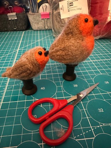 Two felted birds, one larger with an orange chest, accompanied by a pair of red scissors.