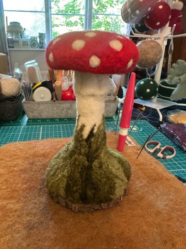 Red and white mushroom with a white stem and green base, crafted from felt.