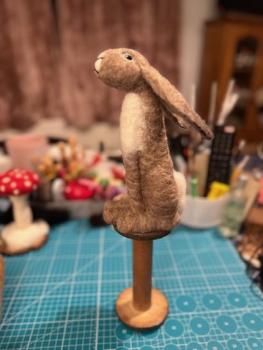 A soft, brown hare figurine sitting on a wooden stand.