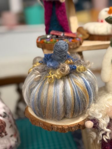 A decorative pumpkin with blue, grey, and gold stripes on a wooden display.