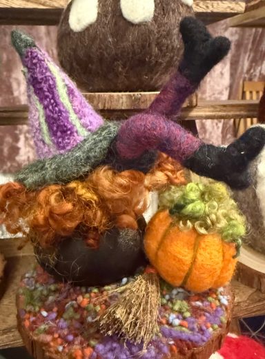 A whimsical witch figure with orange hair, a purple hat, and pumpkins decoratively arranged.