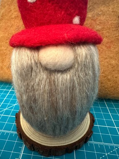 A gnome figure with a red mushroom hat and a grey beard, displayed atop a wooden base.