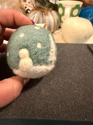 A hand holding a blue and white felted ornament resembling a snowman.