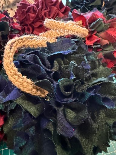 A close-up of fabric flowers in dark red, navy, and green, with a tan crochet band.