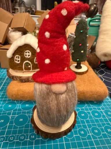A felt gnome with a red polka-dot hat and a grey beard, standing on a wooden base.