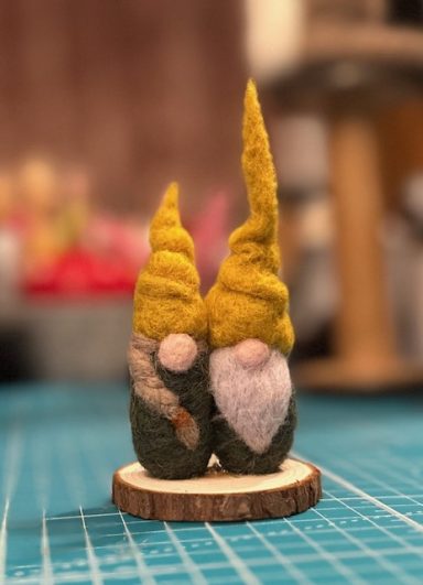 Two small gnomes with yellow hats, standing on a wooden base.