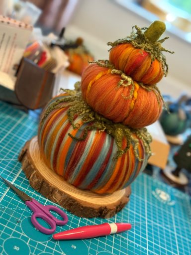 Three stacked, painted pumpkins with decorative foliage, resting on a wooden base.