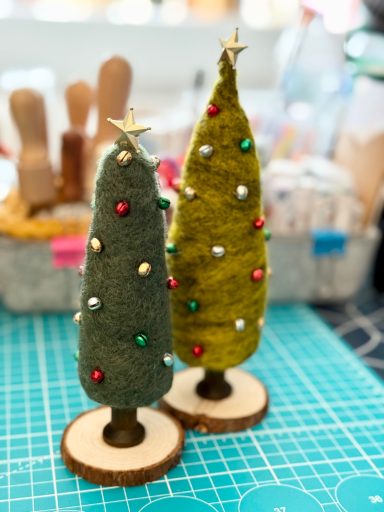 Two small felt Christmas trees on wooden bases, adorned with colourful decorations.