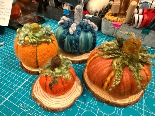 Four decorative pumpkins in various colours and textures, displayed on wooden bases.