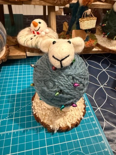 A decorative sheep made of yarn atop a round base with colourful lights.