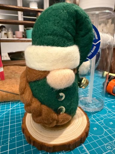 A plush gnome wearing a green hat and brown beard, standing on a wooden base.