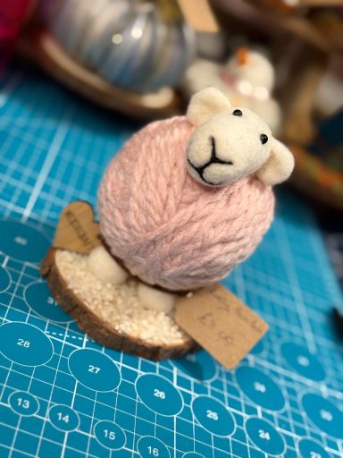 A cute sheep figurine made from pink yarn on a wooden base with labels.